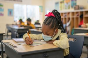  An Indy STEAM Academy student in uniform works at her school desk 