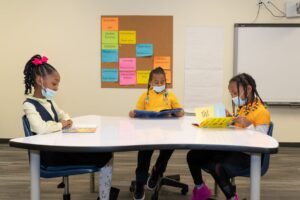 Three Indy STEAM Academy students in yellow uniforms sit around a classroom table reading books independently.