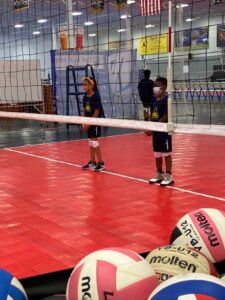 Two Indy STEAM Academy students stand in the gymnasium at a volleyball net in preparation for a game