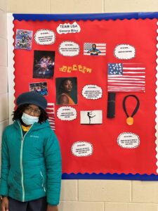 An Indy STEAM Academy student stands in front of her project on Olympic Gymnast Simone Biles. A bulletin board is decorated with pictures and quotes of Biles. 