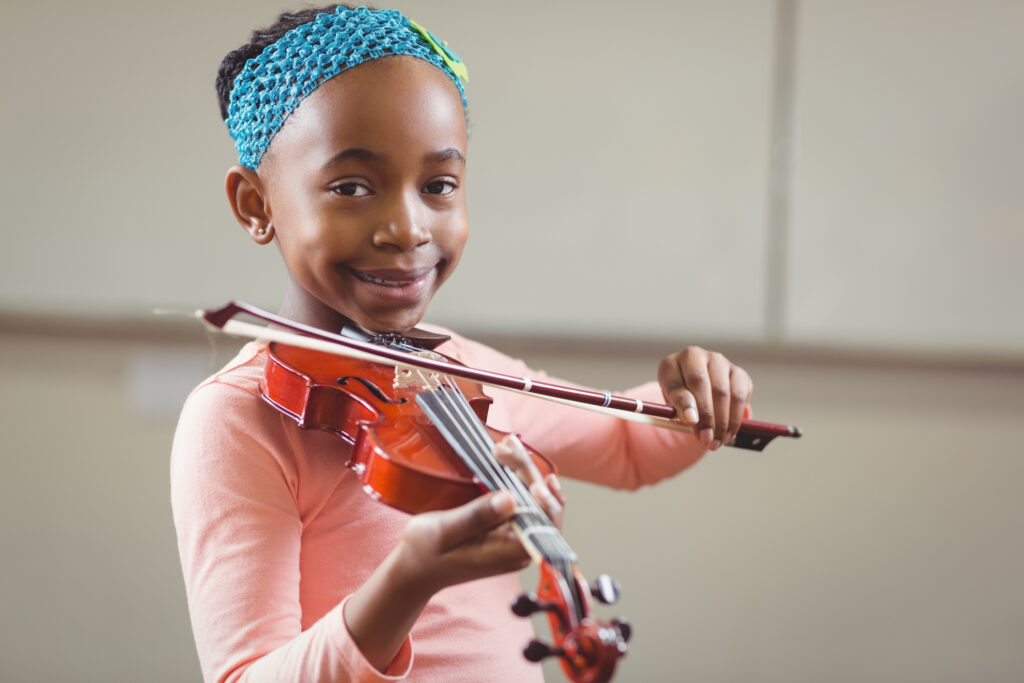Young student smiles while playing a violin.