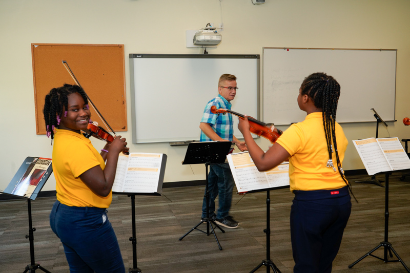 IndySTEAM Academy students in their matching yellow shirts learning how to play the violin